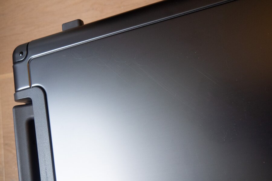 Diagonal and curved scratches cross the grey aluminum carry-on shell beside the recessed handle.