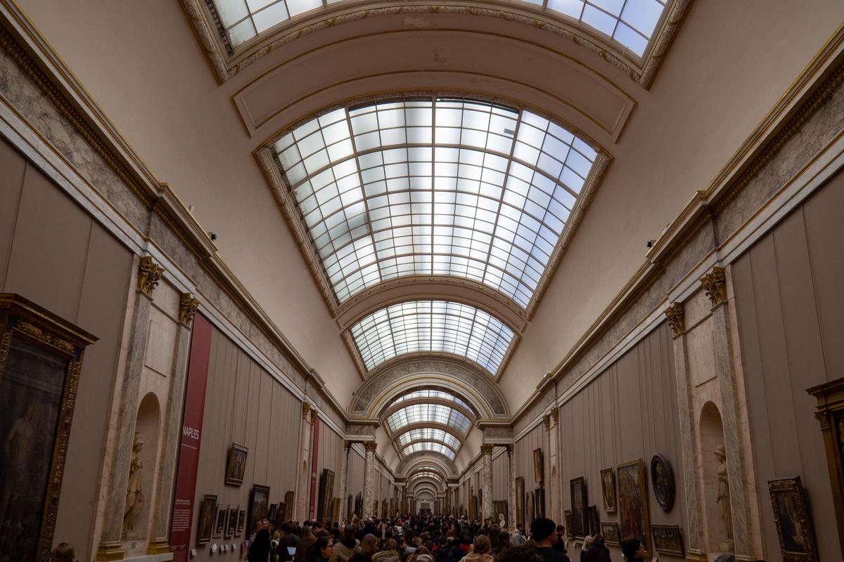Visitors exploring art in the sunny Louvre Museum gallery, Paris