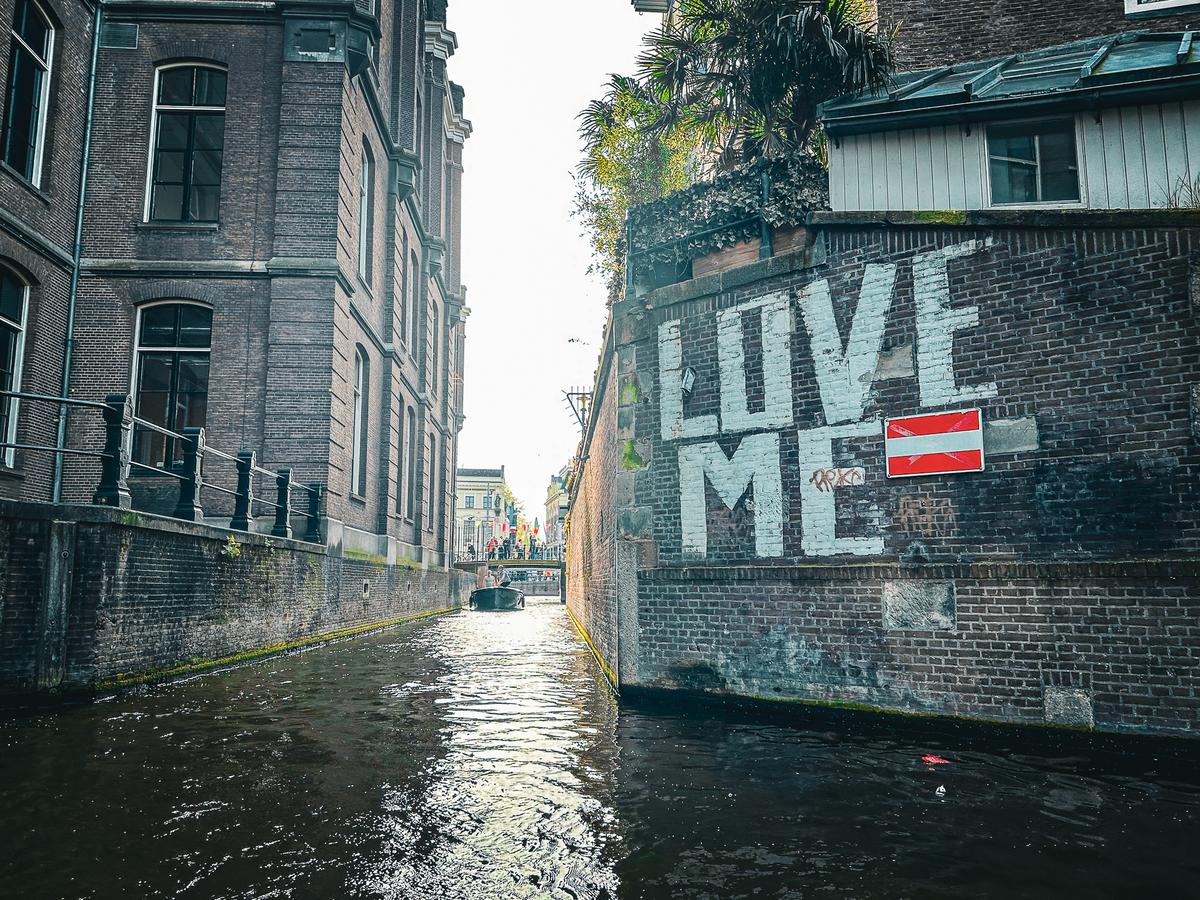 'LOVE ME' graffiti mural on historic Amsterdam canal wall, captured from boat tour perspective