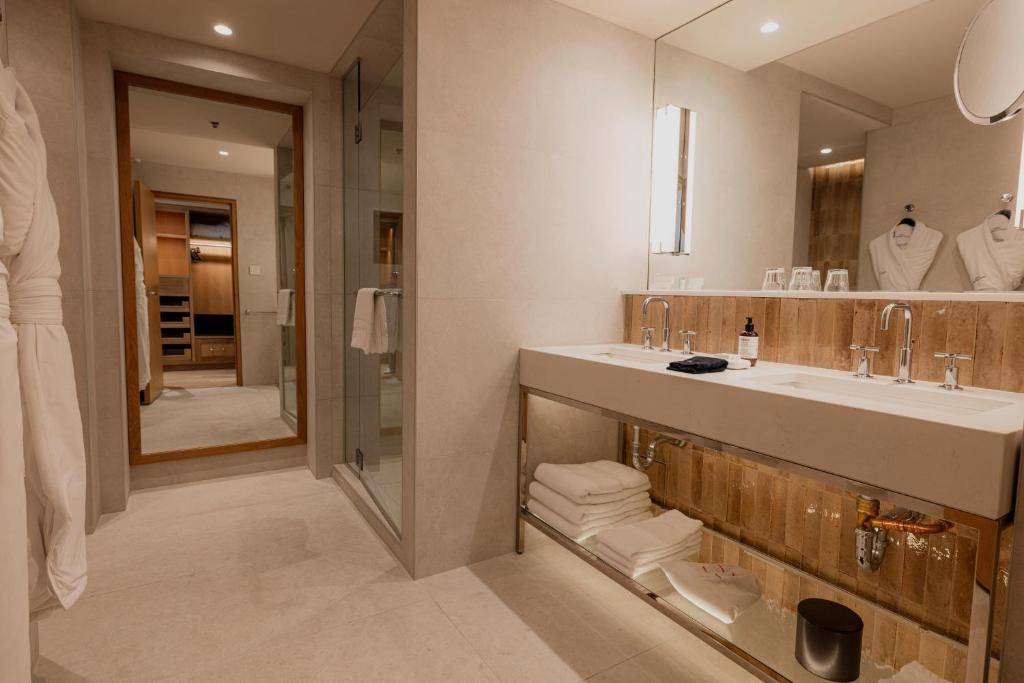 Auberge Saint-Antoine luxurious bathroom with a double vanity, glass shower, full-length mirror, robes, and dressing area.