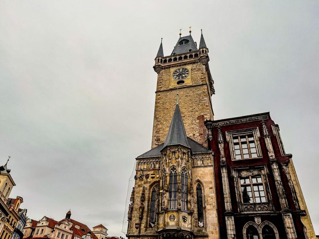 Historic Prague Old Town Hall with Gothic tower and astronomical clock under a cloudy sky.