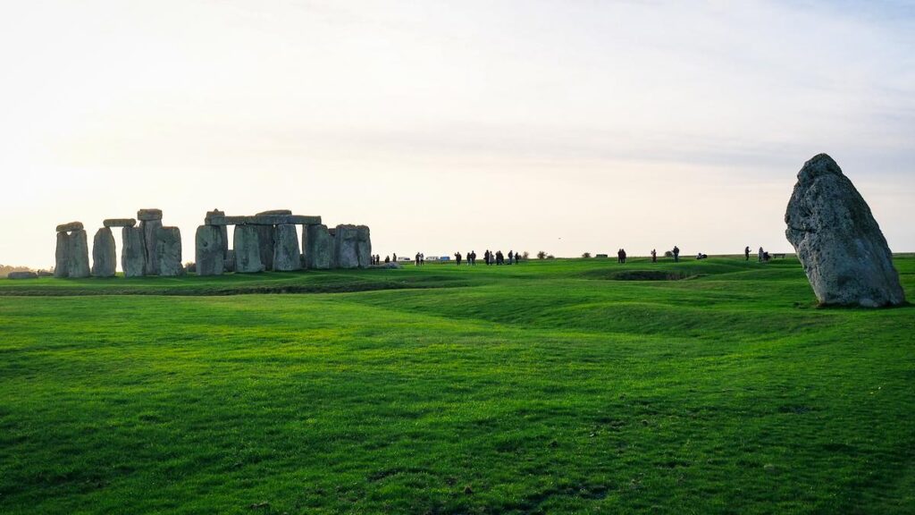 Visitors admire the prehistoric Stonehenge monument under a pastel sunset sky with ancient megaliths standing tall on the Salisbury Plain, England.