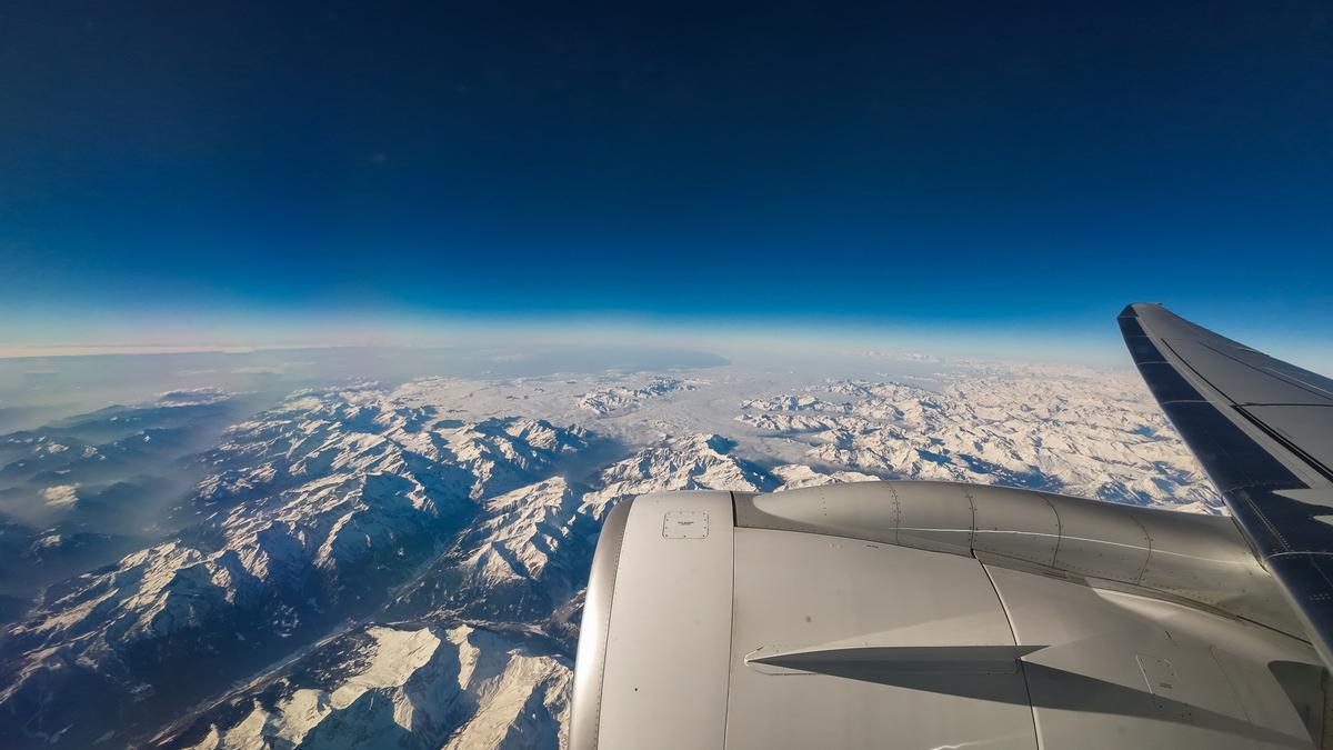 Aerial view of majestic Swiss Alps with snow-covered peaks and airplane wing, evoking travel exhilaration.