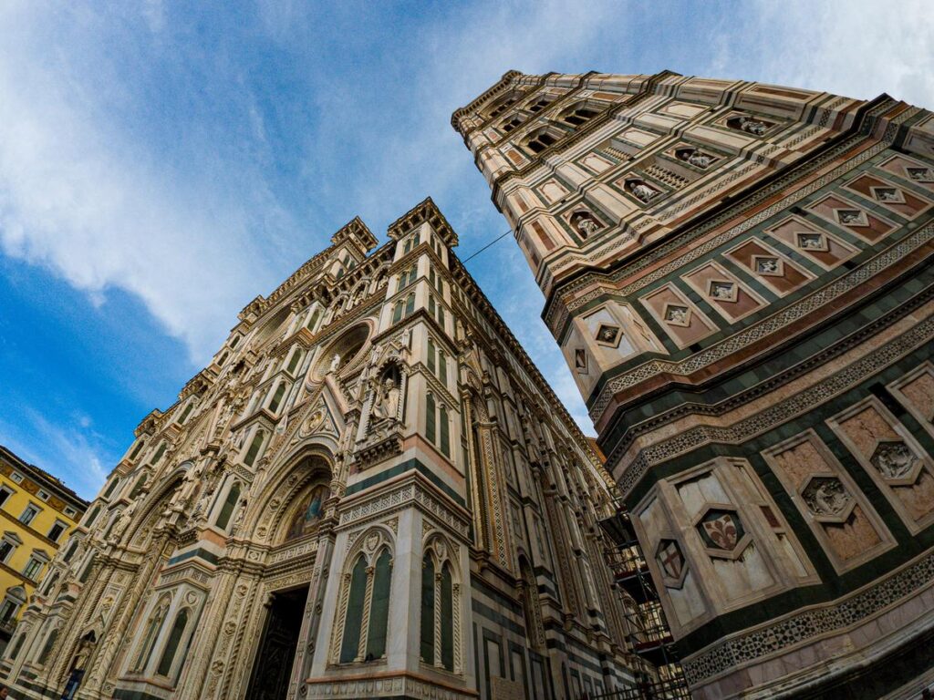 Wide-angle view of Santa Maria del Fiore Cathedral's elaborate facade and bell tower against a clear blue sky.