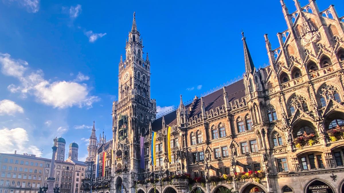 Majestic view of New Town Hall, Marienplatz, Munich, Germany – historical Gothic facade, vibrant flags, clear skies, famous clock tower.