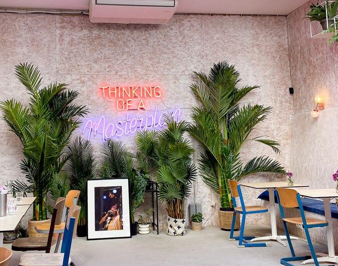 Interior of Moak Pancakes Amsterdam with vibrant plants, neon sign, and cozy seating