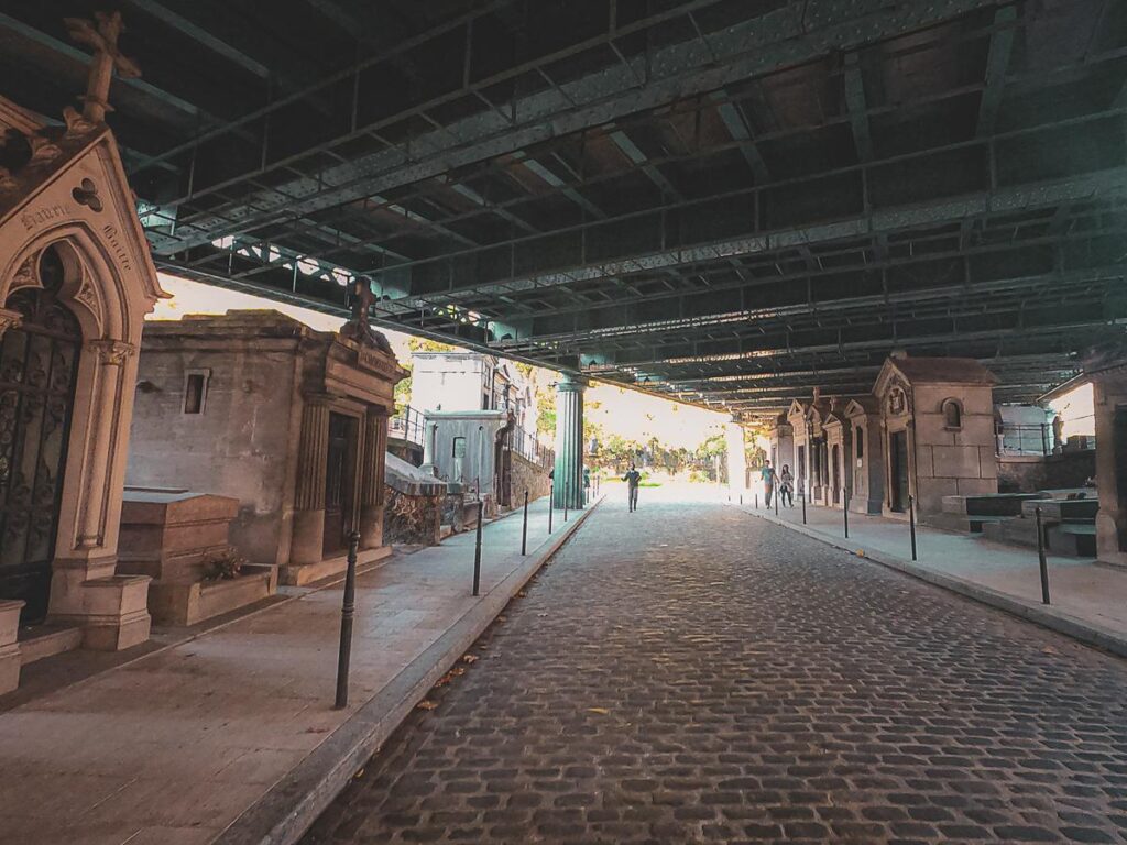 Montmartre Cemetery under Overpass: Serene cobblestone path with mausoleums and crypts, Paris
