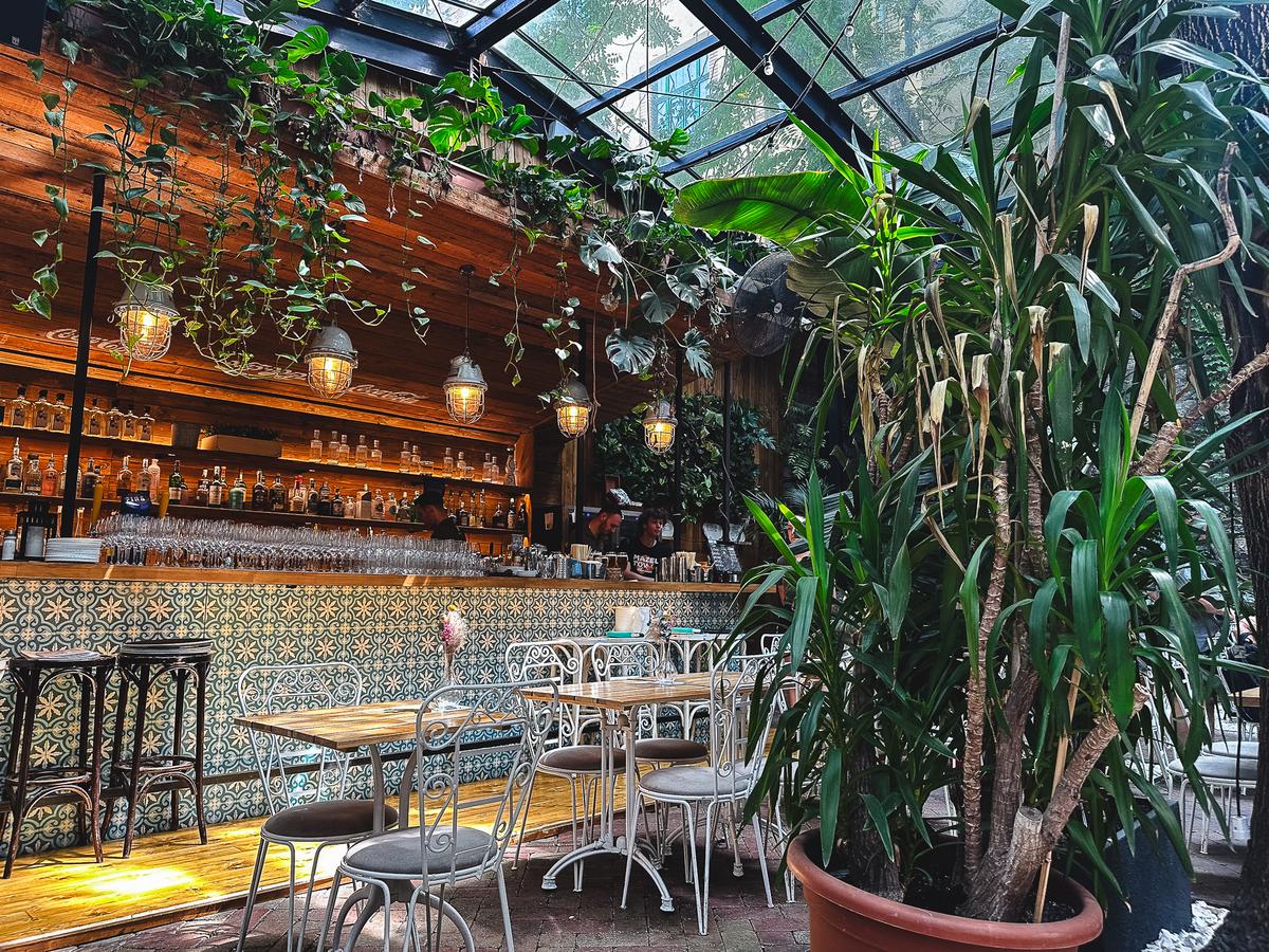 Interior of a Budapest Israeli restaurant with botanical theme, wooden bar, patterned tiles, and abundant plants.