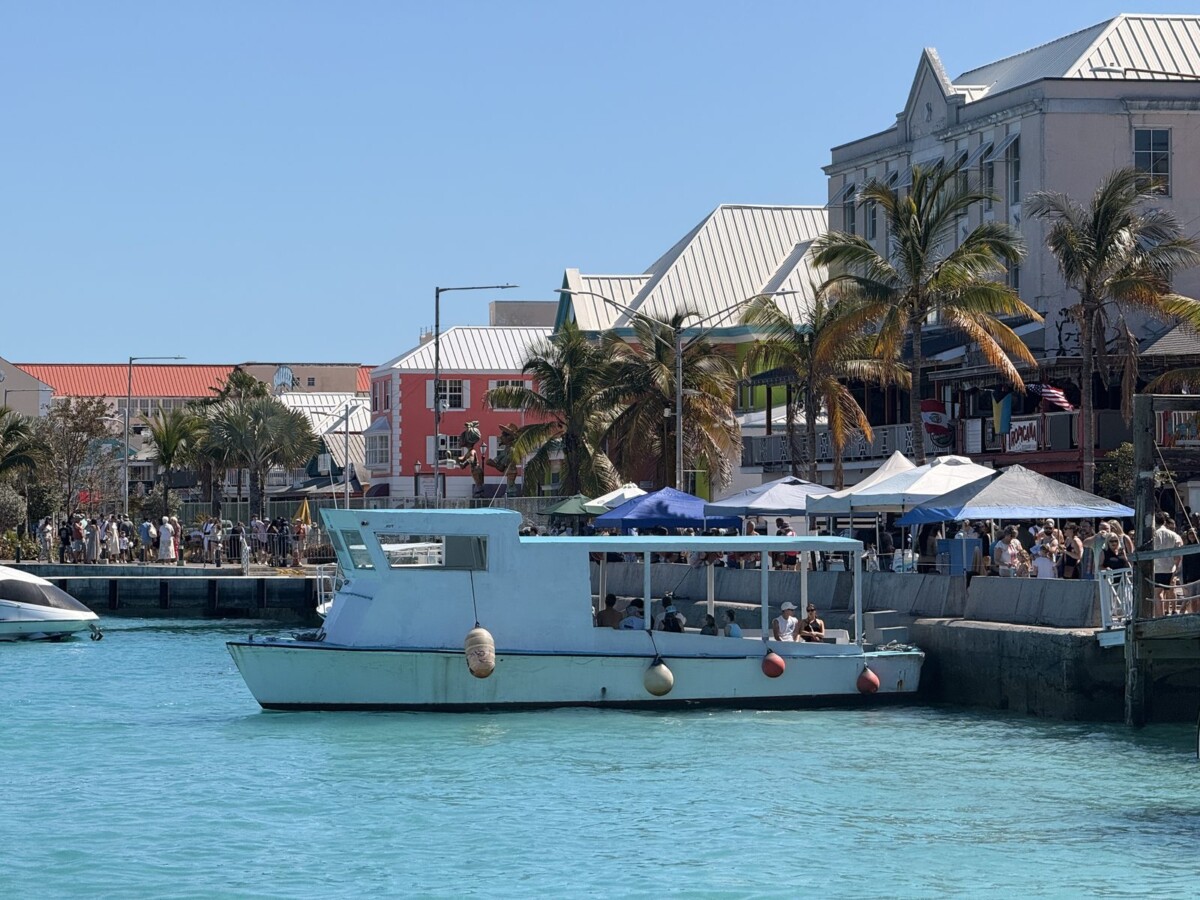 Turquoise water, tour boats, and pastel waterfront buildings with palm trees at Nassau's cruise port harbour