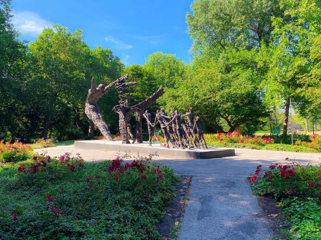 National Slavery Monument in Oosterpark, Amsterdam, vibrant daylight, figures breaking free from oppression, lush surroundings.