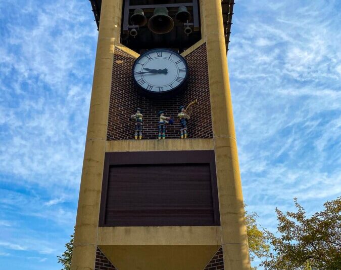 The Glockenspiel in New Ulm, Minnesota, featuring a clock face and ornate bells under a blue sky, with traditional figurines on display.