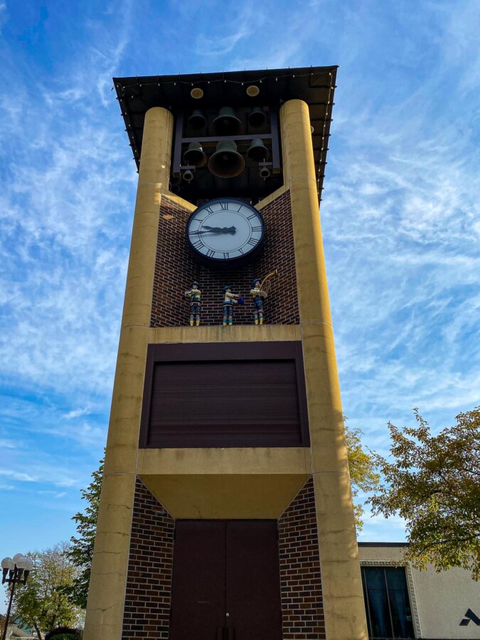 The Glockenspiel in New Ulm, Minnesota, featuring a clock face and ornate bells under a blue sky, with traditional figurines on display.