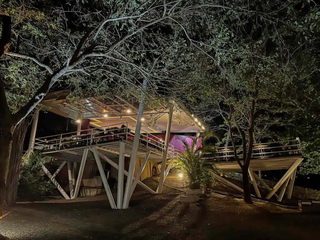 Night view of Ginger Restaurant and Bar in Guanacaste, Costa Rica, beautifully lit with a warm glow amidst tropical trees, showcasing its unique structural design and inviting dining ambiance.