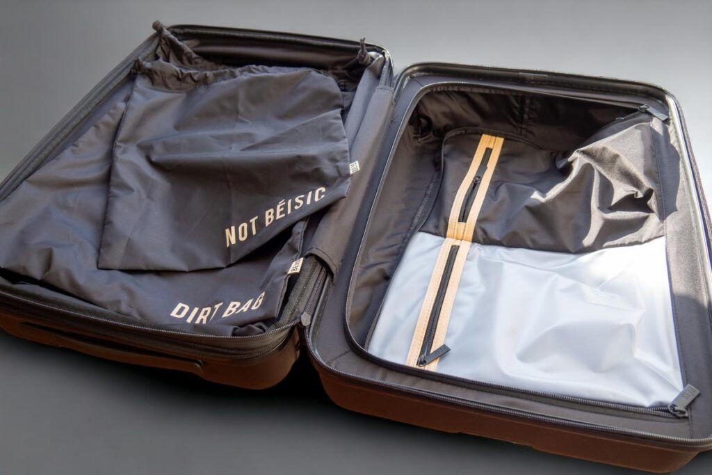 Open Beis carry-on roller suitcase with dual compartments and DIRT BAG and NOT BEISIC labels