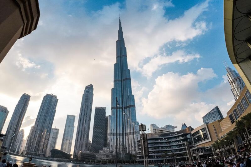 Wide-angle shot of Burj Khalifa towering above downtown Dubai at sunset with clouds in the sky, reflecting the city's dynamic mix of modern architecture and leisure attractions.