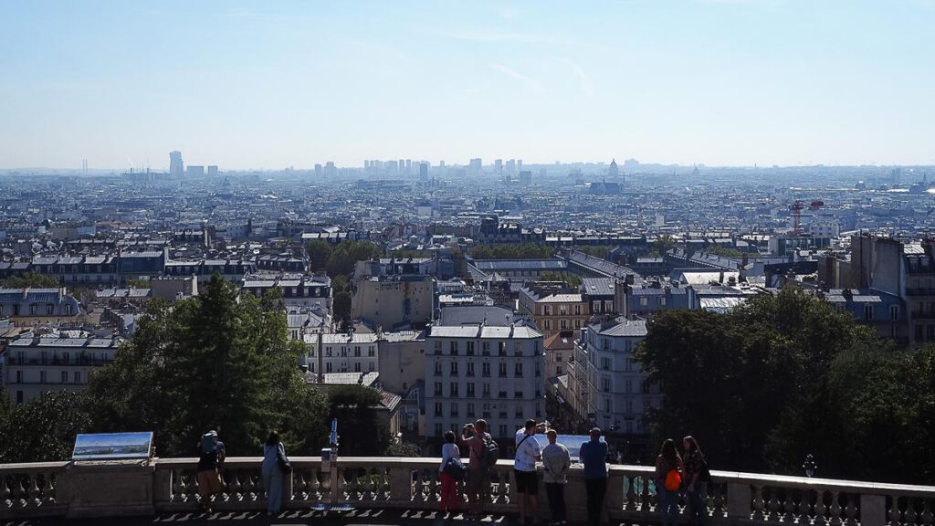 Panoramic view of Paris skyline from Montmartre overlook with tourists admiring the cityscape on a clear day.