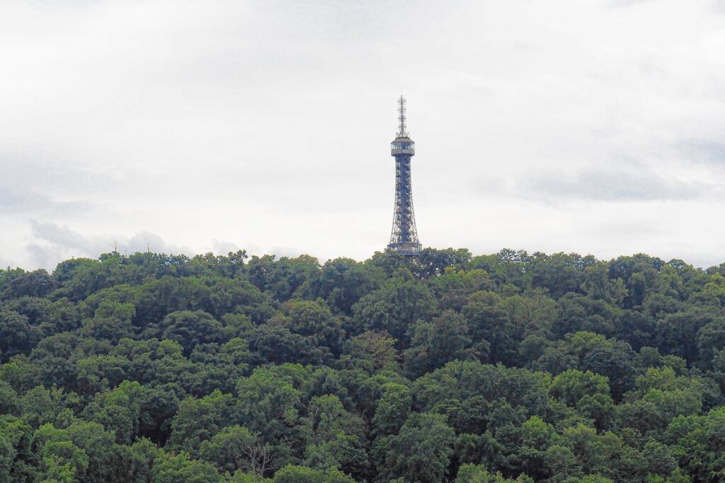 The steel structure of Prague's Petřín Tower rising above a dense canopy of trees on Petřín Hill, reflecting Czech Republic's natural and architectural heritage.