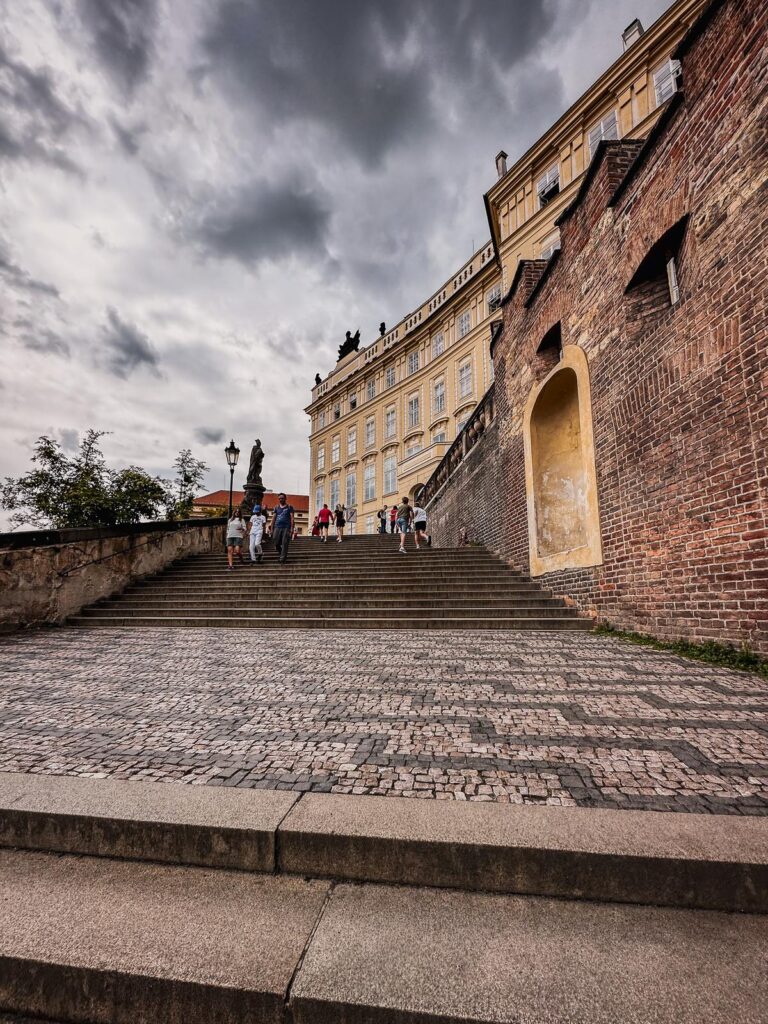 Tourists ascending steps to Prague Castle under moody skies