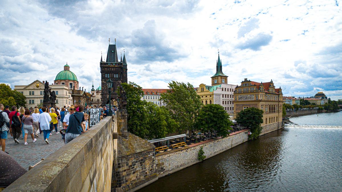 Charles Bridge in Prague with tourists, vendors, and iconic architecture under a dynamic sky.