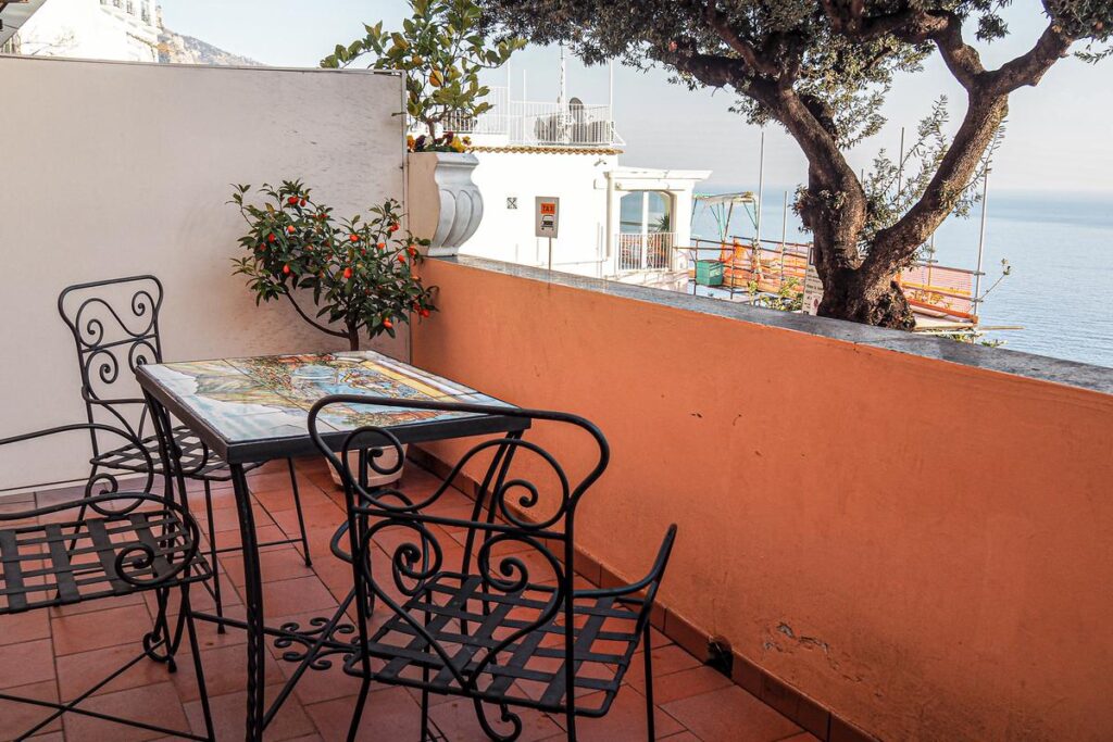 Private patio at Hotel Villa Gabrisa, Positano, Italy. Wrought-iron table, chairs, sea view, citrus tree, serene ambiance.