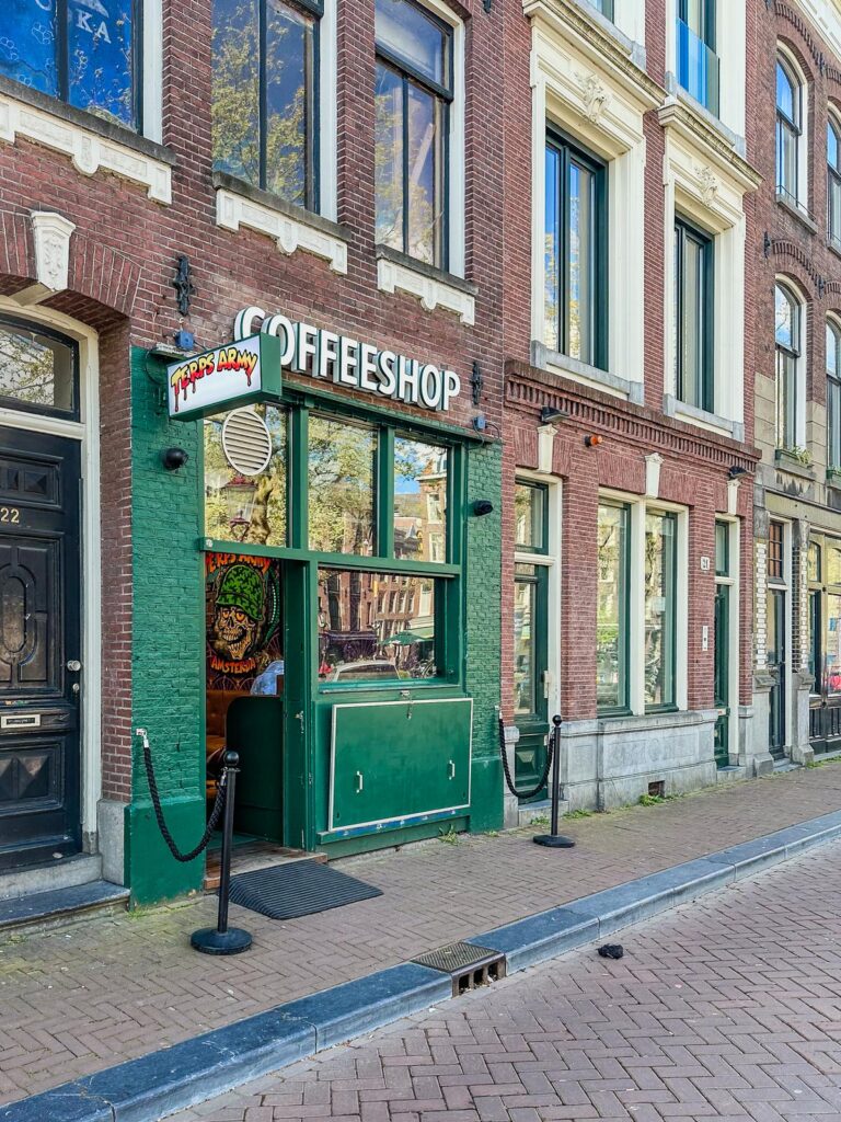 Quaint and Charming Coffeeshop Facade in Amsterdam's City Centre: Traditional Dutch architecture with inviting green entrance and Coffeeshop sign against clear blue sky.