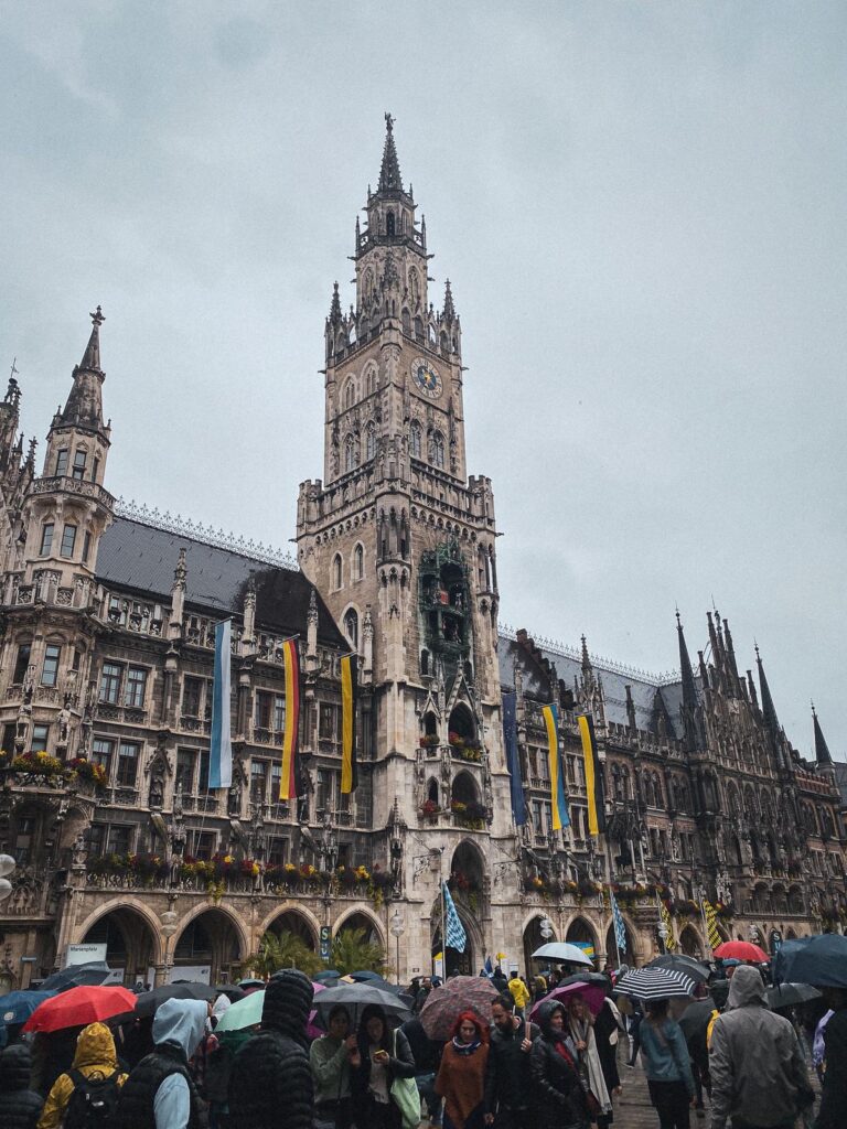 Rainy Oktoberfest celebrations at Marienplatz, Munich - vibrant crowd with colorful umbrellas and New Town Hall in the background.
