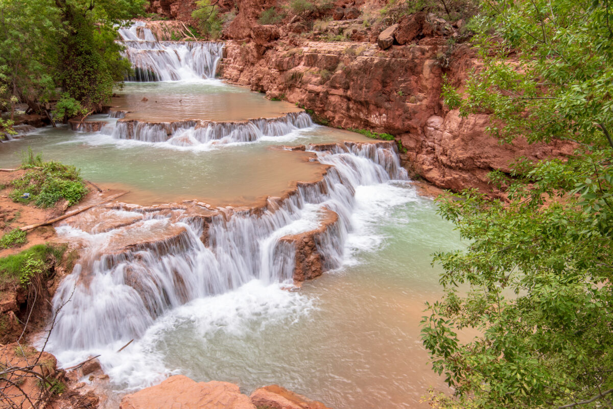 Beaver Falls Havasupai: turquoise terraced waterfalls cascade through red canyon rock amid lush greenery.