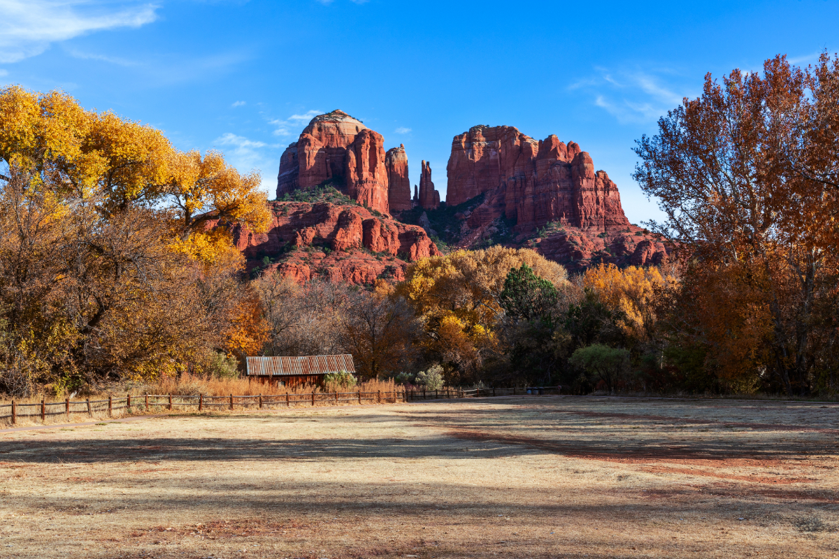 Cathedral Rock and red rock formations and autumn foliage in a tranquil landscape with rustic structures.