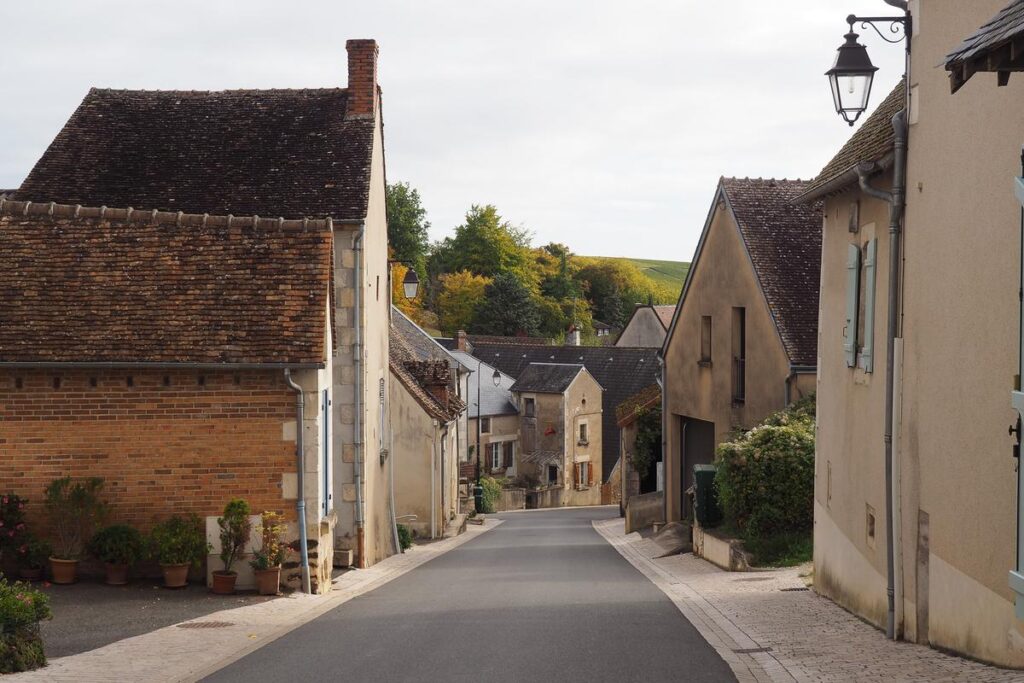 Rustic charm of Sancerre, France: picturesque street with traditional houses, potted plants, and lush vineyards in the distance.