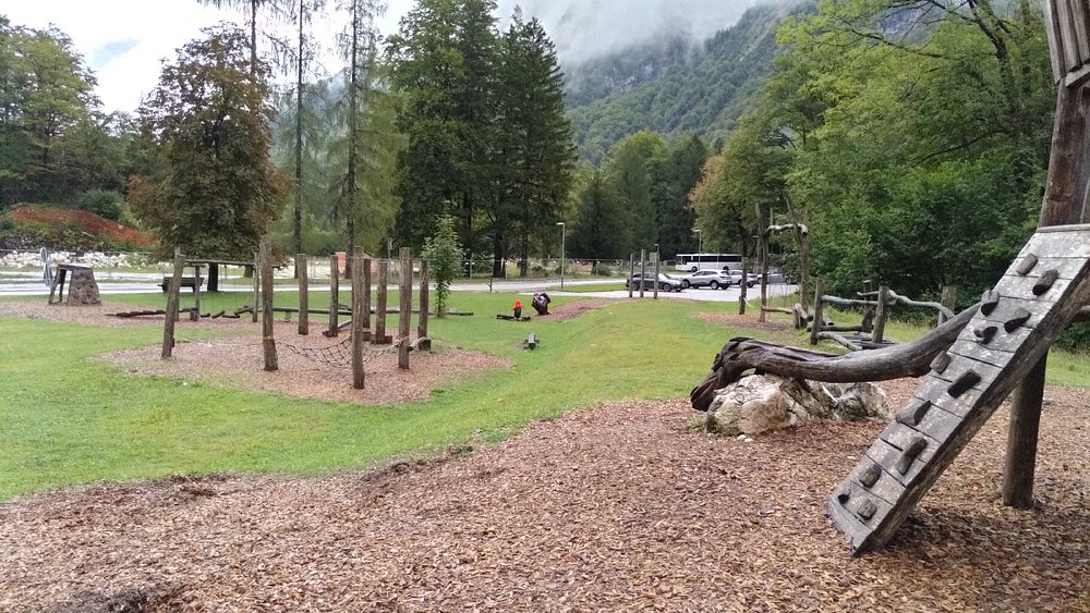 Zlatorog Fairy Trail nature playground with timber structures, woodchip ground, misty mountains, and a lone visitor.