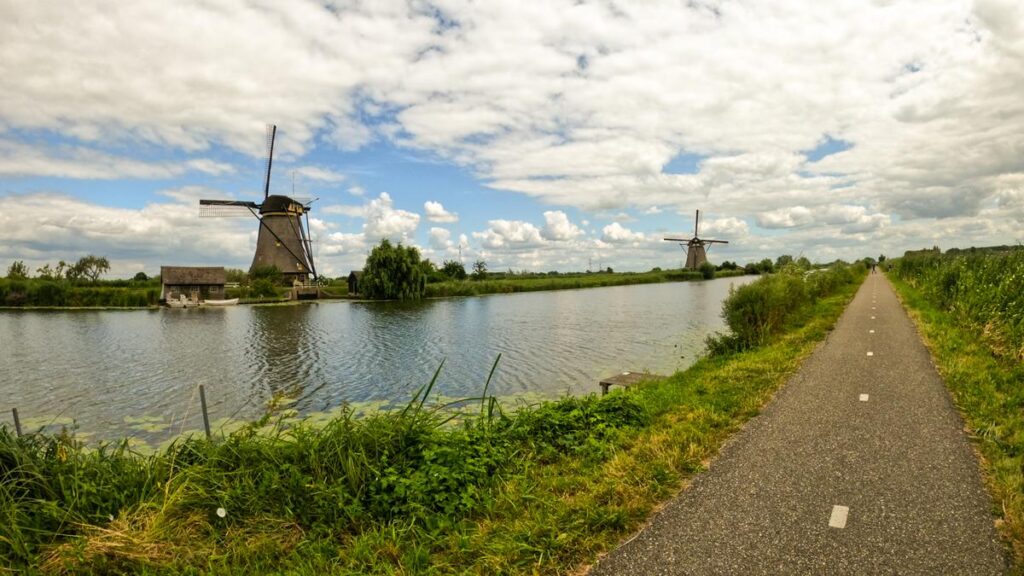 Scenic Bike Path with Traditional Dutch Windmills in Kinderdijk, Netherlands, sRGB photo of lush greenery, windmills, and bike trail