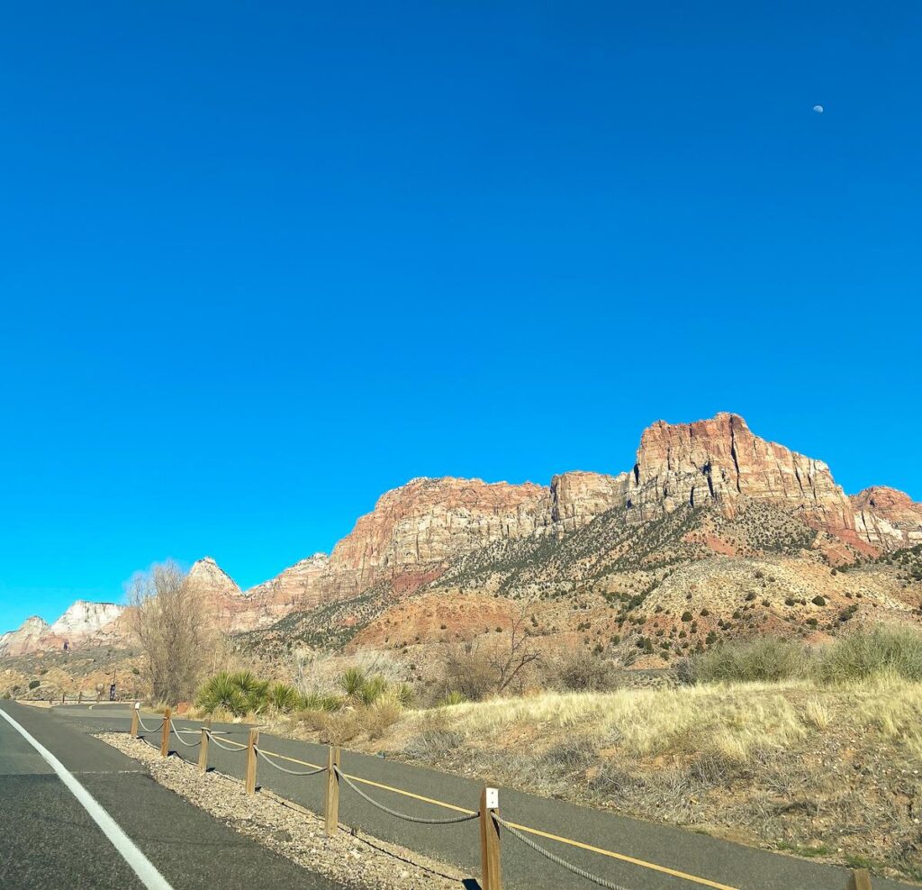 Pristine bike path and road near majestic red rock cliffs of Zion National Park under a bright blue sky