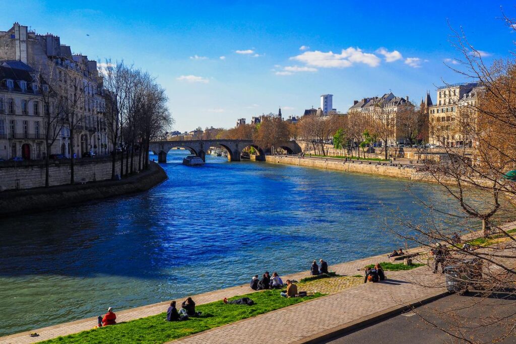 Sunny Seine River with Parisians relaxing by historic buildings
