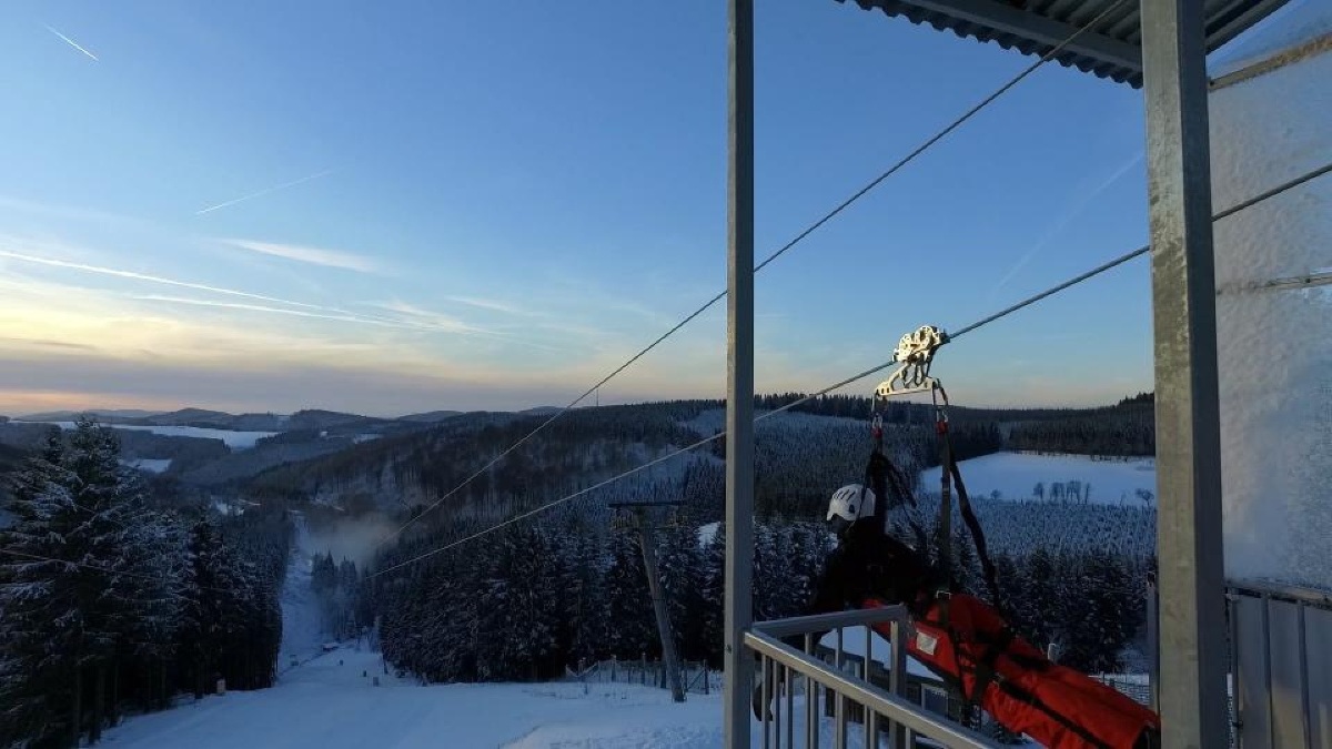 Snowy mountain zip line in Germany above forested ski slopes.