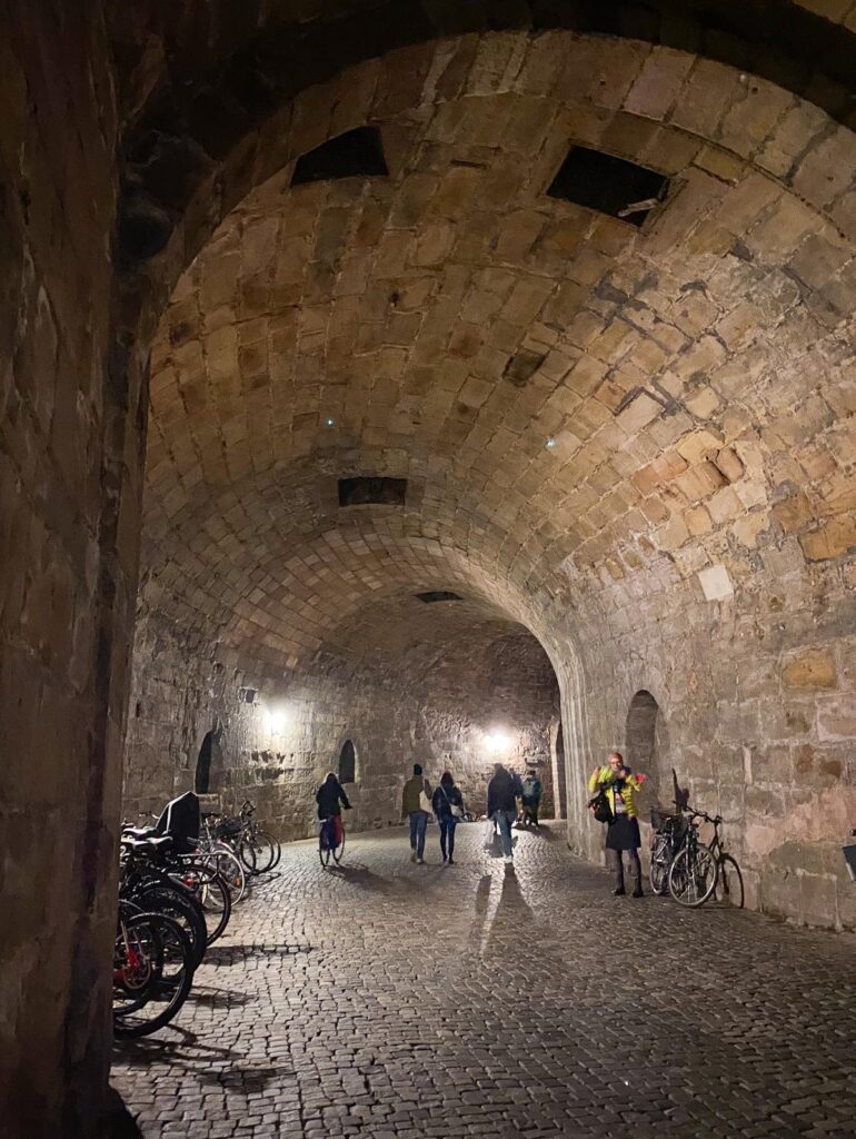 Stone tunnel under Imperial Castle of Nuremberg, subterranean passage with cobblestone pavement, pedestrians, and bicycles.