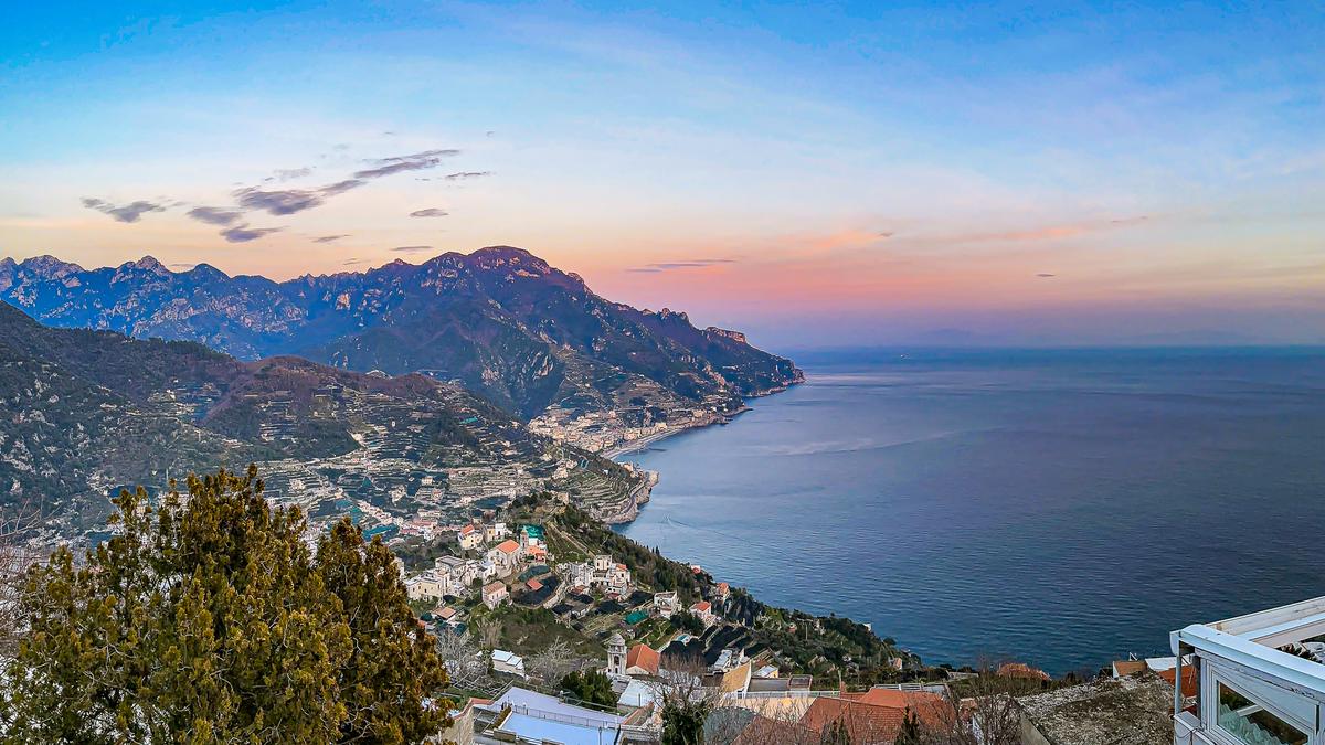 Breathtaking sunset view over Amalfi Coast from Ravello, Italy: Cliffside villages, terraced hills, and the Tyrrhenian Sea at dusk.