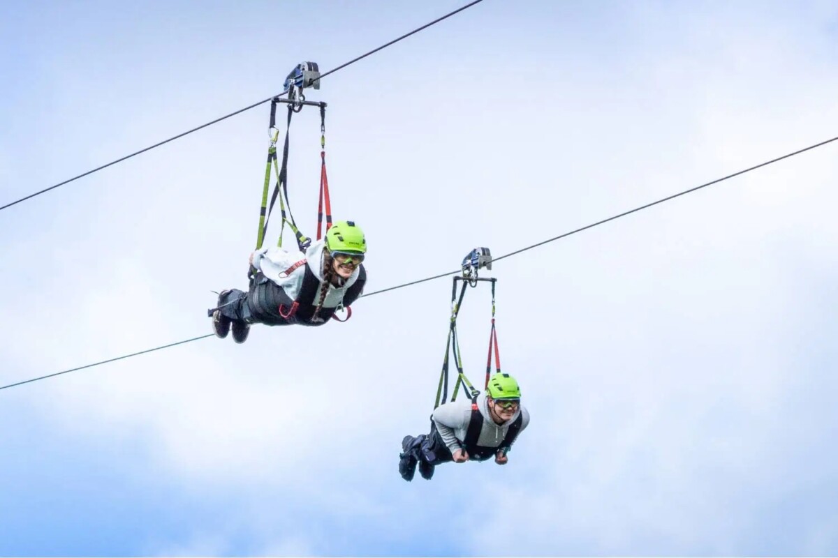 Superman zip line riders in Germany soaring through cloudy sky.