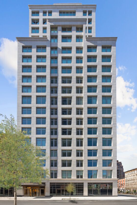 Modern high-rise with pale grid facade, glass windows, terraced crown, and urban street view.