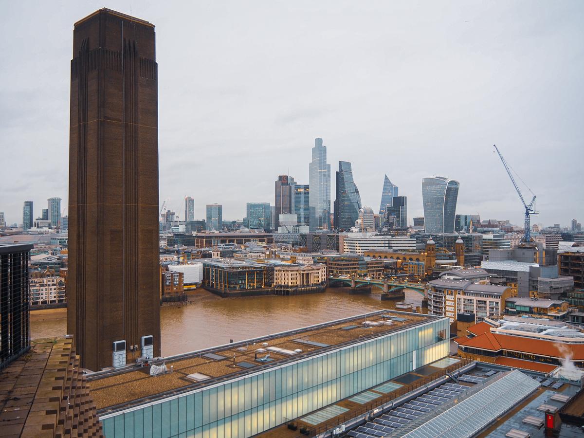 Tate Modern London skyline with historic chimney, modern buildings, and overcast sky. GPS coordinates: 51.507585, -0.0994.