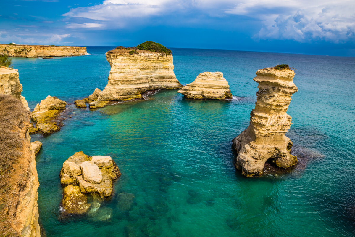 Based on the image descriptions and the provided filename and image title, the alt text for this image should be "View of Torre dell'Orso beach, Lecce, Italy with crystal-clear water and rocks of various sizes."