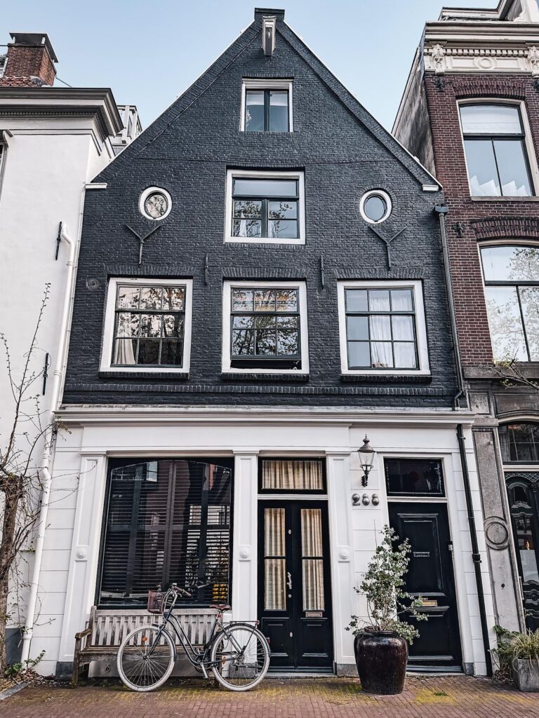 Traditional Amsterdam house with black facade, Dutch gable, and bicycle, showcasing iconic architecture and local culture.