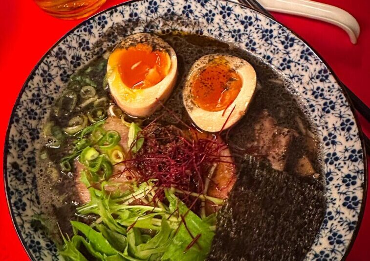 Traditional Japanese ramen bowl from Kodawari Yokoch Paris with soft-boiled eggs, pork slices, and fresh vegetables in a patterned bowl with a beer