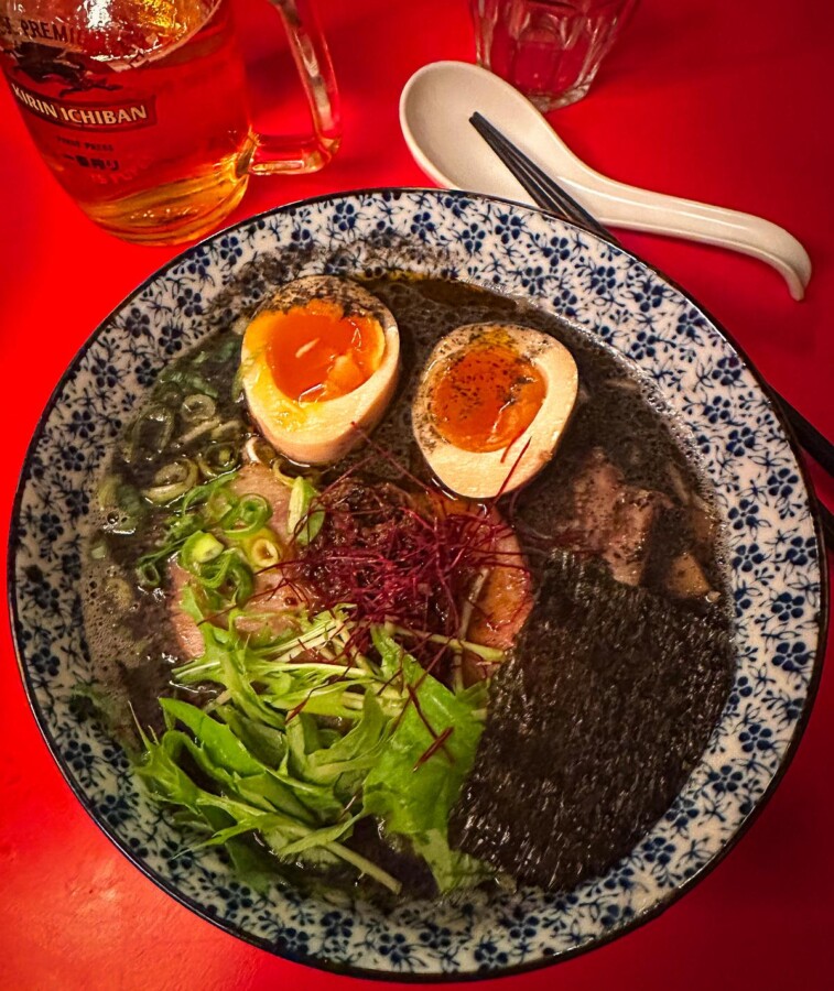 Traditional Japanese ramen bowl from Kodawari Yokoch Paris with soft-boiled eggs, pork slices, and fresh vegetables in a patterned bowl with a beer