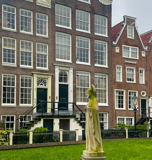Tranquil courtyard at Historical Begijnhof, Amsterdam: Dutch houses, green lawn, weathered statue.