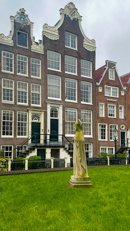 Tranquil courtyard at Historical Begijnhof, Amsterdam: Dutch houses, green lawn, weathered statue.
