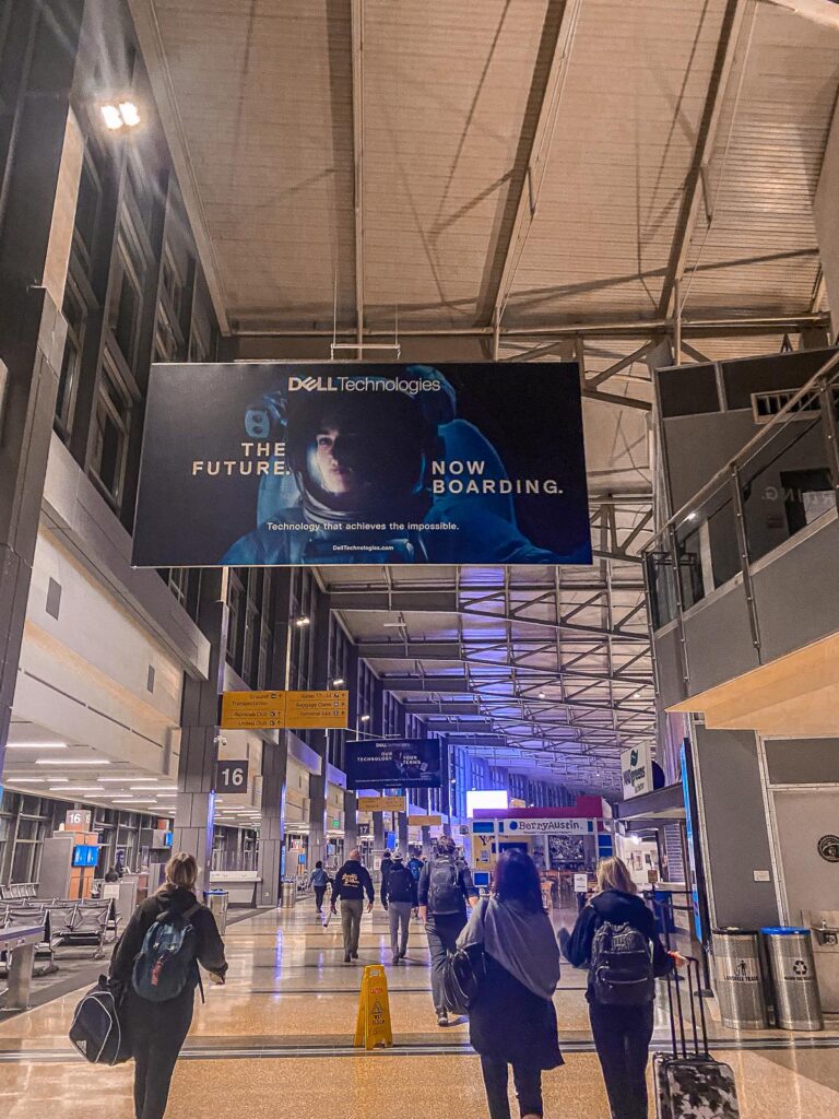Travelers with luggage in Austin-Bergstrom International Airport at dusk, showcasing the airport's tech industry connection and vibrant atmosphere.
