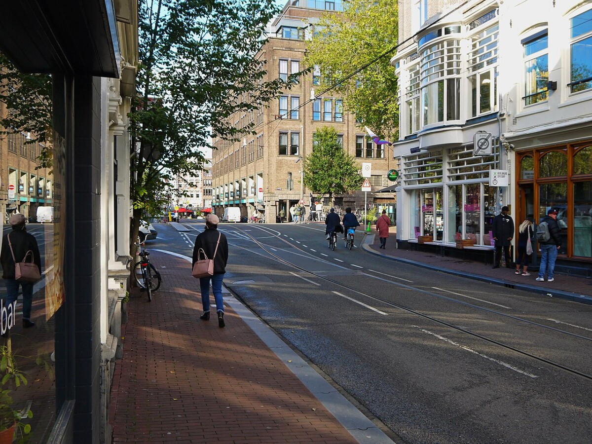Amsterdam shops along tram tracks with cyclists on a quiet urban street.