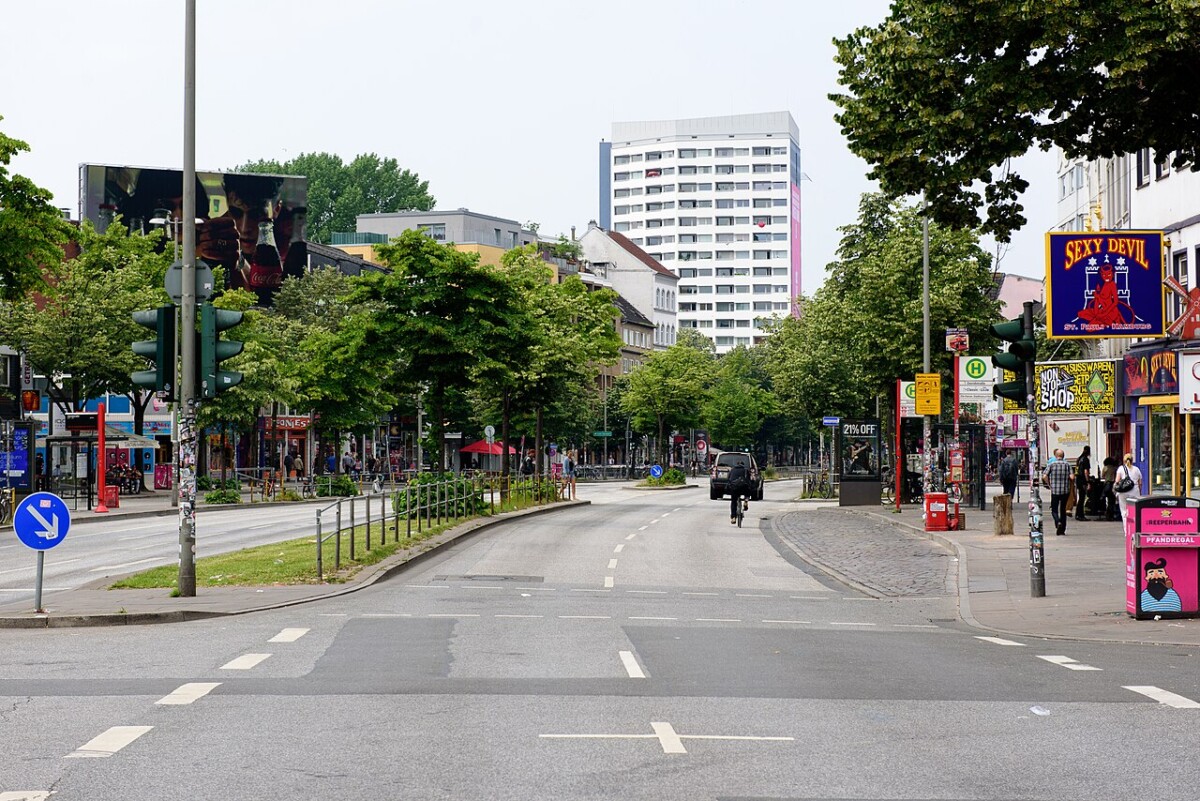 Hamburg landmarks and monuments along a tree-lined street intersection with shops and cyclists.