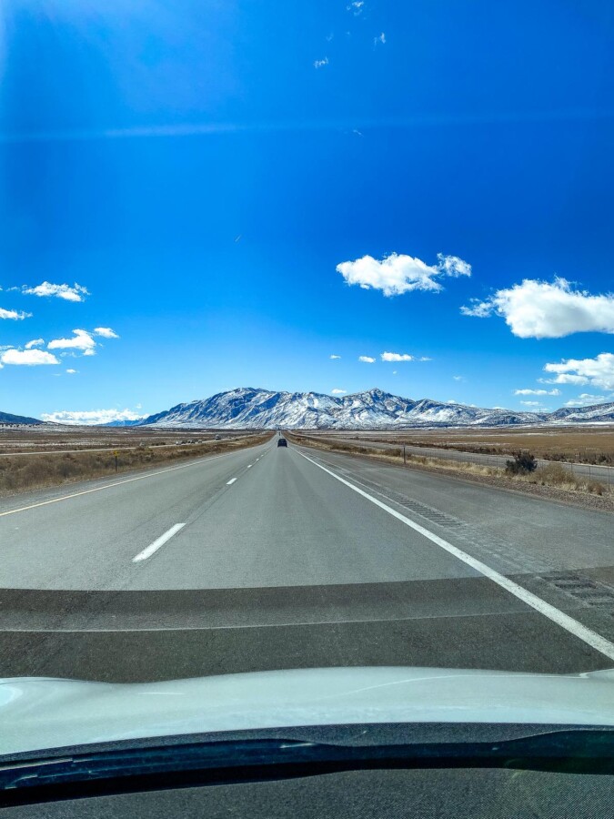 Alt text: Car driving towards towering mountains under clear blue sky, embodying road trip adventures in the American Southwest.