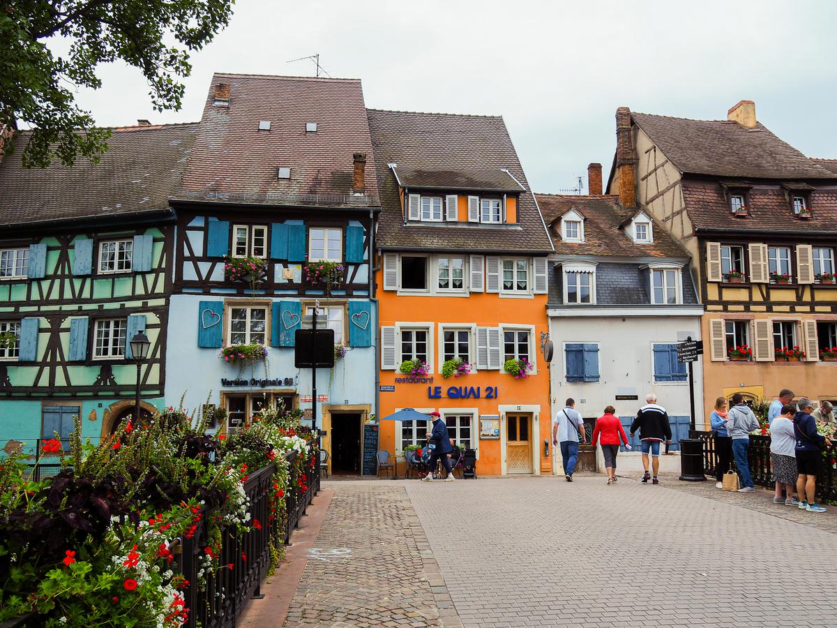 Vibrant photograph of traditional Alsatian architecture in Colmar, France, capturing the essence of the historic district with colorful half-timbered buildings, flower-lined streets, and a quaint cobblestone pathway.